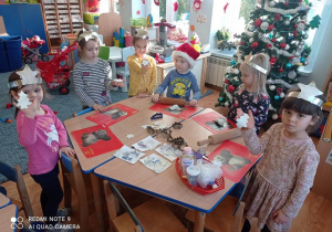 Dzieci przy stoliku prezentują wycięte foremkami ozdoby z masy porcelanowej.